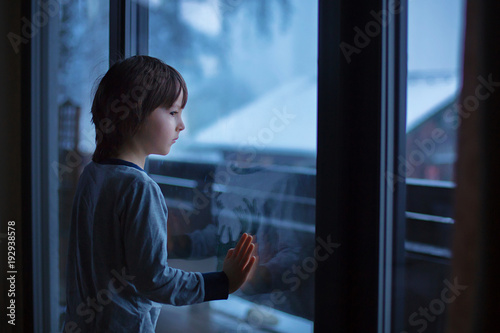 Preschool boy, sitting by the window in living room, looking at a snowy landscape Free Download Preschool boy, sitting by the window in living room, looking at a snowy landscape - GFXLoad