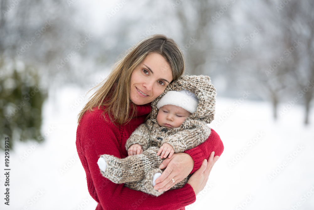 Beautiful mother and cute baby boy in knitted onesie, having taken their beautiful winter outdoor portrait Beautiful mother and cute baby boy in knitted onesie, having taken their beautiful winter outdoor portrait