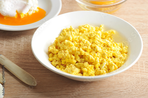Scrambled eggs from chicken eggs in a white deep plate. Close-up. Light wooden background.