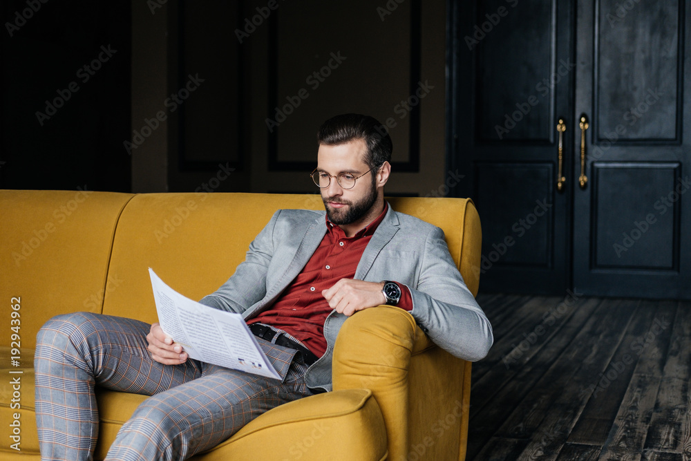 stylish handsome man reading newspaper and sitting on couch