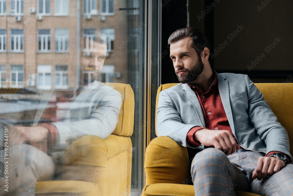 Handsome bearded man sitting on yellow couch at window with reflection Handsome bearded man sitting on yellow couch at window with reflection