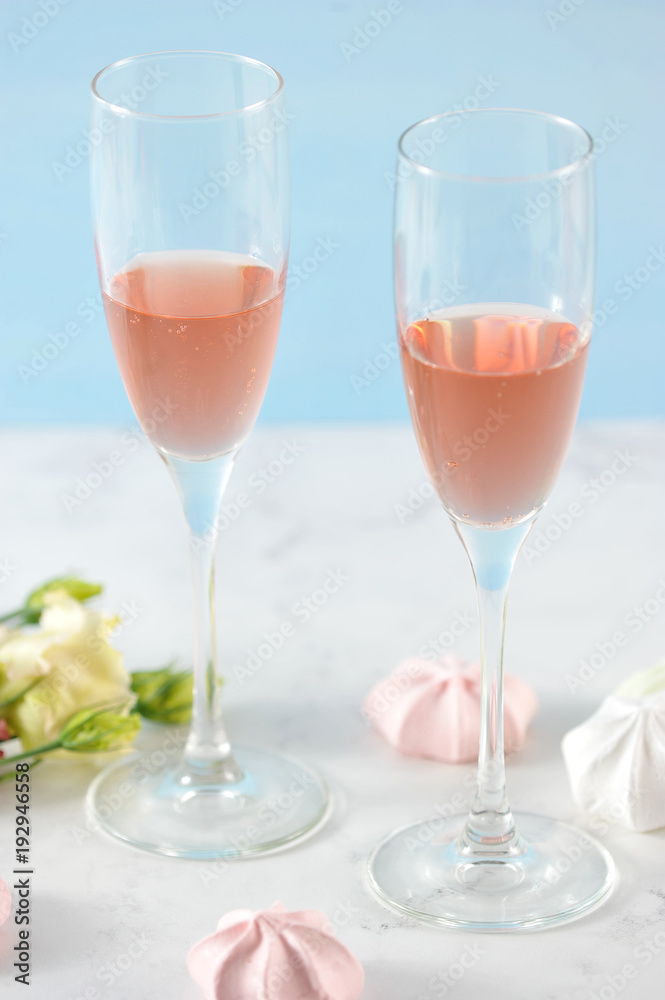 Two glasses with pink wine. In the frame flowers and meringue in light pink colors. Light background. Close-up. Vertical orientation of the frame. Two glasses with pink wine. In the frame flowers and meringue in light pink colors. Light background. Close-up. Vertical orientation of the frame.