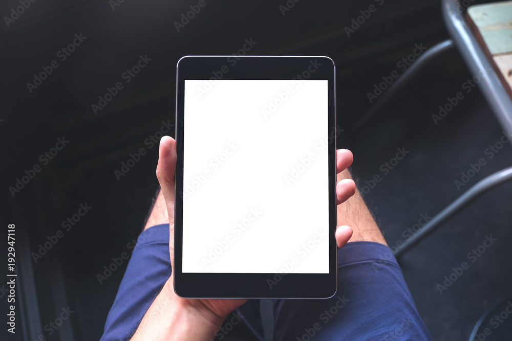Mockup image of a man's hand holding black tablet pc with blank white screen on thigh Mockup image of a man's hand holding black tablet pc with blank white screen on thigh