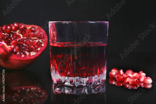 Glass with pomegranate juice Pomegranate seeds and Beautiful ripe pomegranate on black mirror background with place for copy space. photo