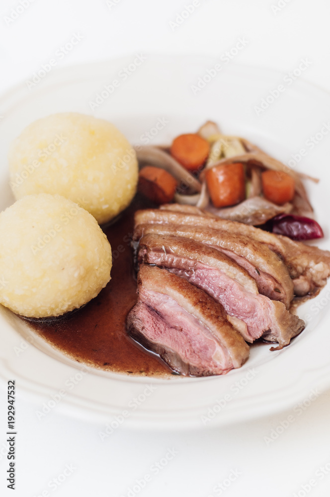 Plate with roasted duck breast, roasted vegetables such as carrots, red onions and scallions with traditional Franconian or Bavarian potato dumplings and gravy as typical German sunday roast dish