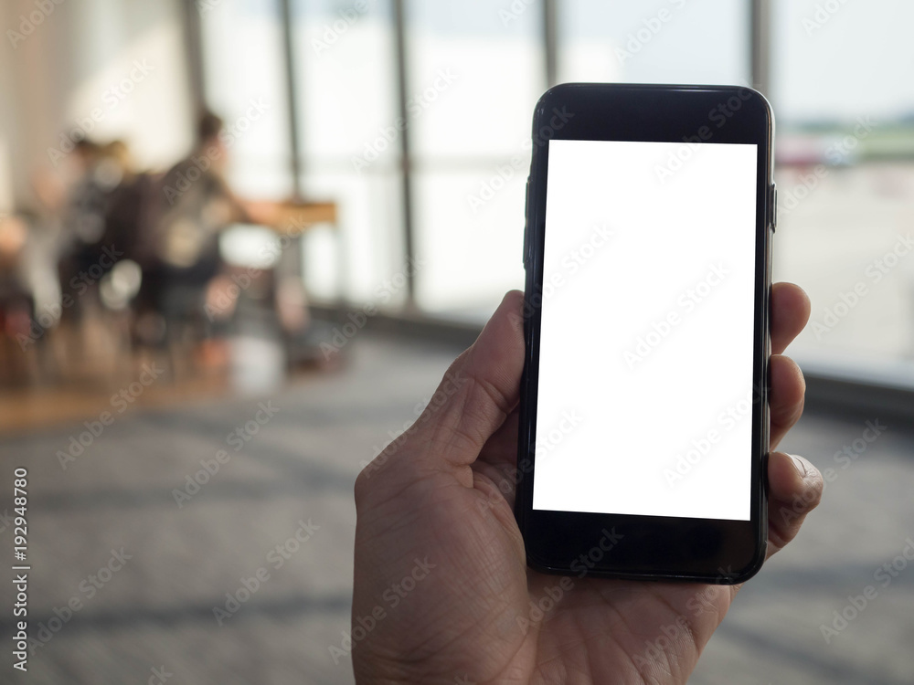 Closeup image of hand holding black mobile phone with blank white screen in airport terminal background Closeup image of hand holding black mobile phone with blank white screen in airport terminal background