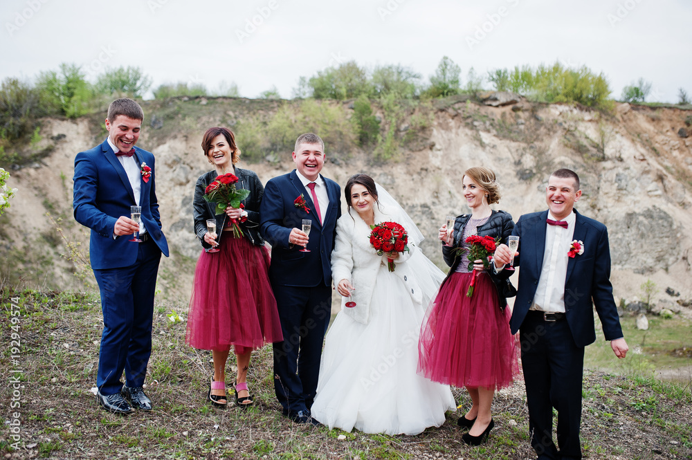 Fantastic wedding couple and bridesmaids with groomsmen drinking champagne in sand quarry.