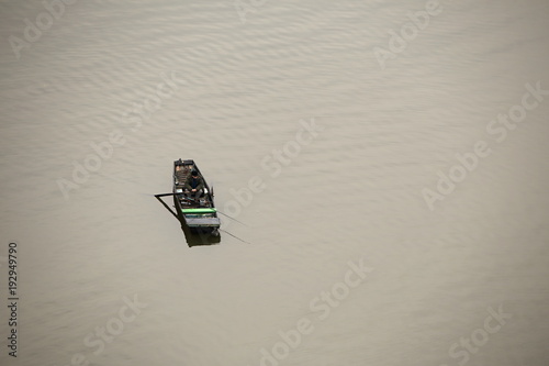 Fishing boat with man sitting in it on the calm brownish water surface