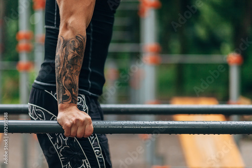 Young caucasian athlete in black sportwear and tattoos, training outdoor and posing