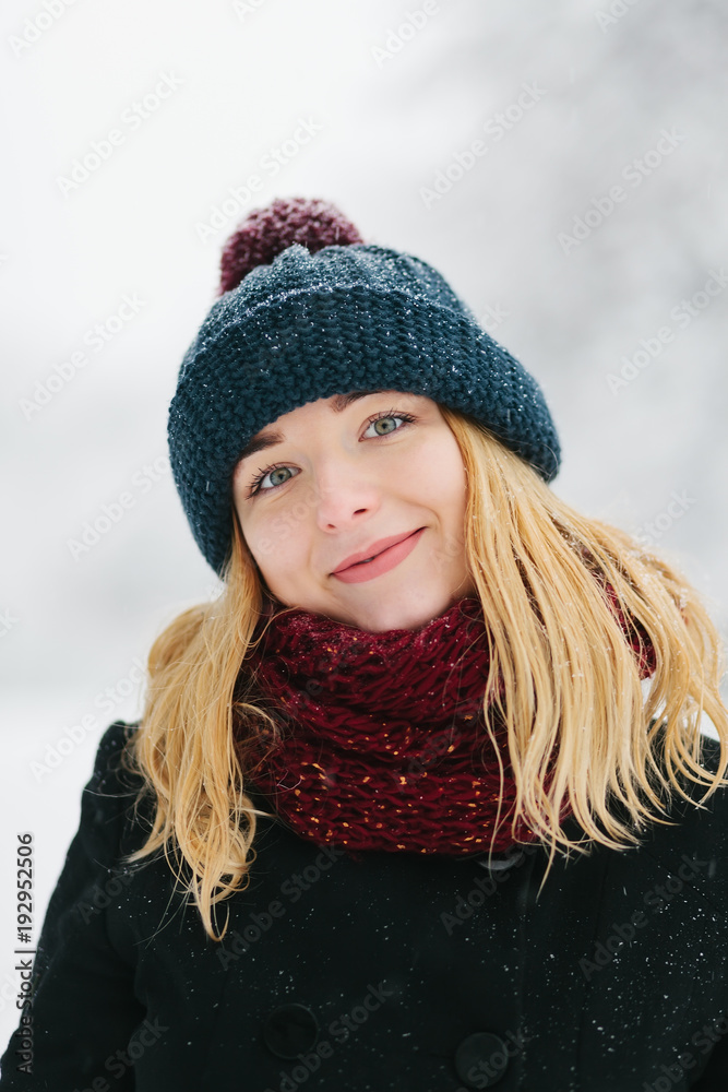 Young caucasian blonde girl in black coat and red knitted scarf walks in winter park Young caucasian blonde girl in black coat and red knitted scarf walks in winter park