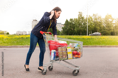 Attractive young caucasian brunette drives shopping cart to her car