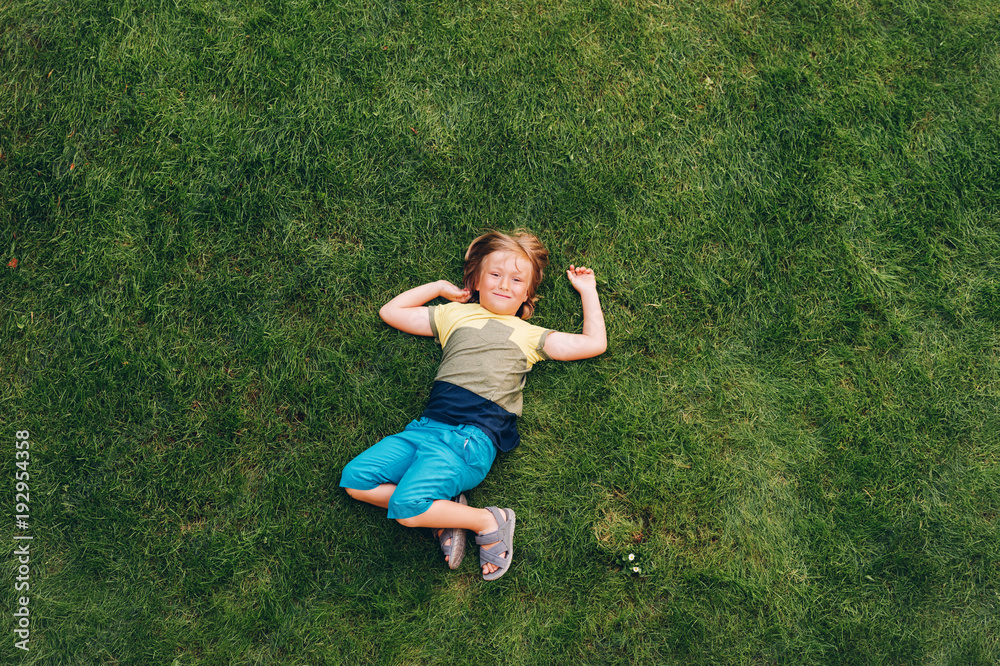 Happy child having fun outdoors. Kid playing in summer park. Little boy lying on green fresh grass, top view