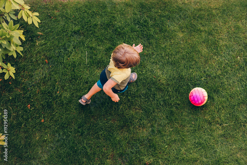 Schilderij op canvas Little boy playing with the ball outside on green lawn, top view