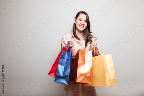 Beautiful smiling girl looks inot a camera holding shopping boxes