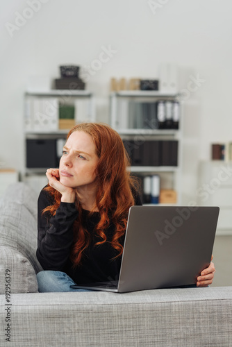 Young thoughful woman sitting with laptop on sofa © contrastwerkstatt
