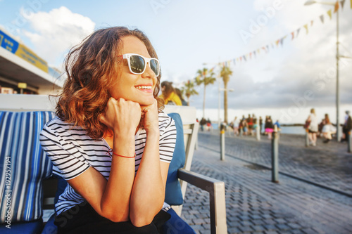 young beautiful woman girl in a striped T-shirt sitting in a street cafe smiling, seaside town, vacation and travel