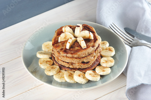 Buckwheat pancakes are lined with a slide on a plate. Pancakes are decorated with a banana with chocolate syrup. Around the pancakes on a plate lined with bits of banana. Wooden background. Close-up.