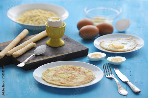 A set of dishes made from chicken eggs. Omelette, scrambled eggs, soft-boiled egg, two halves of a hard-boiled egg, fried eggs, a cup with a raw egg. In the frame of the shell and a few chicken eggs.