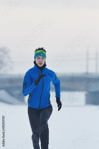 Young male athlete running in winter through the snow