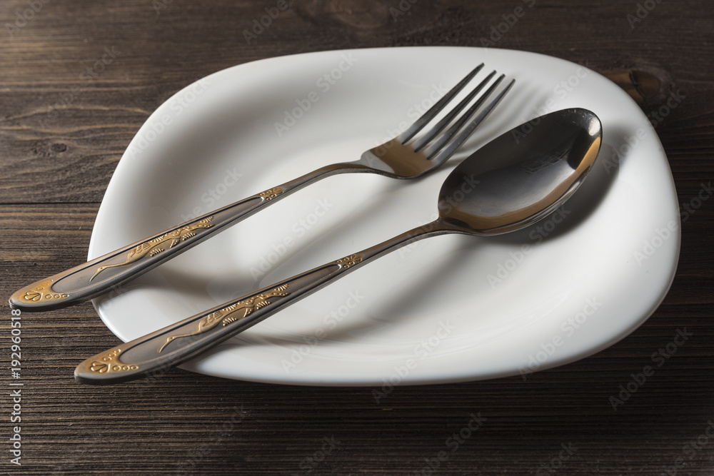 Fork, spoon and white plate on a dark wooden background Fork, spoon and white plate on a dark wooden background