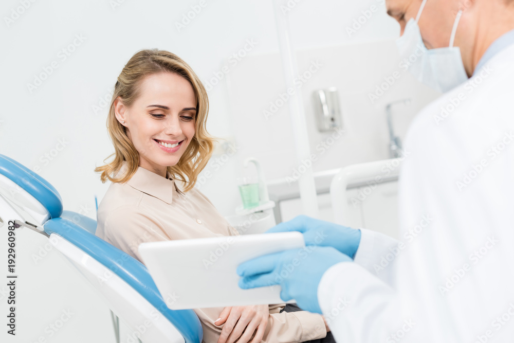 Doctor and smiling patient looking at tablet screen in modern dental clinic Doctor and smiling patient looking at tablet screen in modern dental clinic