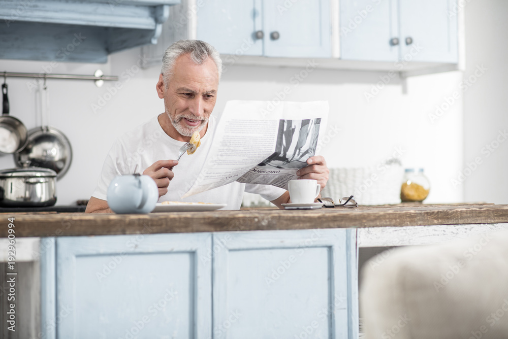 Favorite food. Cheerful man expressing positivity while reading article and eating omelet