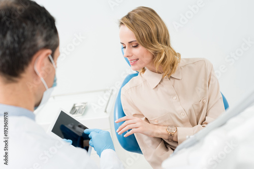 Male doctor and female patient looking at tablet screen in modern dental clinic