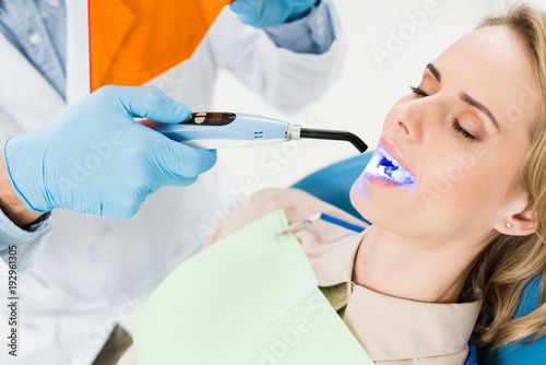 Dentist using uv lamp to treat patient teeth in modern dental clinic