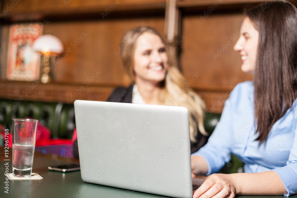 Pretty smiling girls in background working on a coputer in foreground in a cafe Pretty smiling girls in background working on a coputer in foreground in a cafe