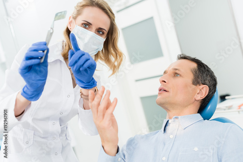 Female dentist showing male patient x-ray in modern dental clinic