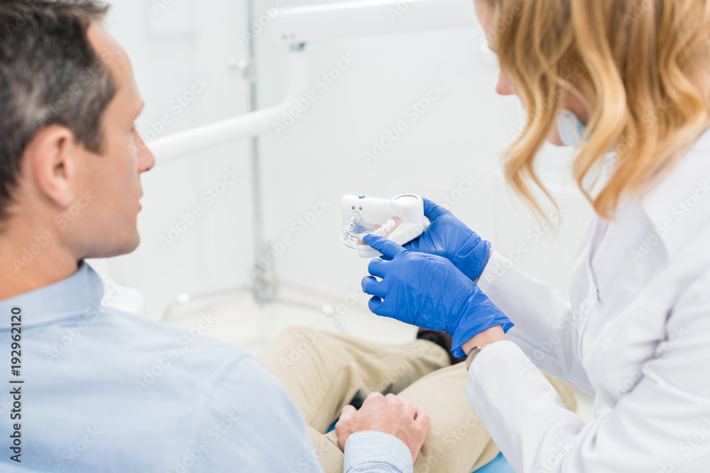 Doctor showing jaws model to male patient in modern dental clinic Doctor showing jaws model to male patient in modern dental clinic