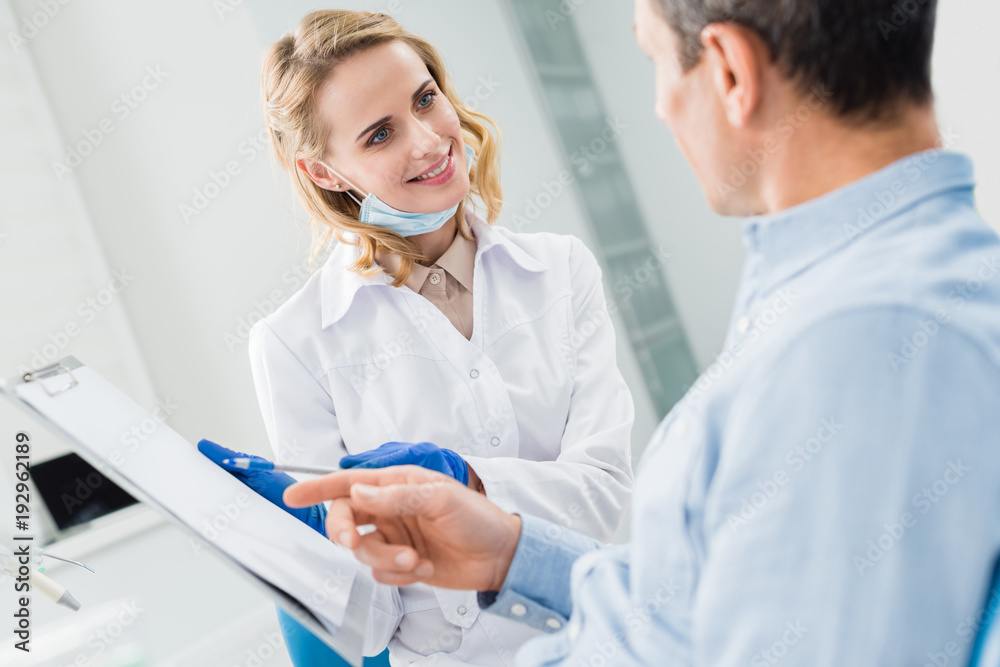Man consulting with female dentist recording diagnosis in modern clinic Man consulting with female dentist recording diagnosis in modern clinic