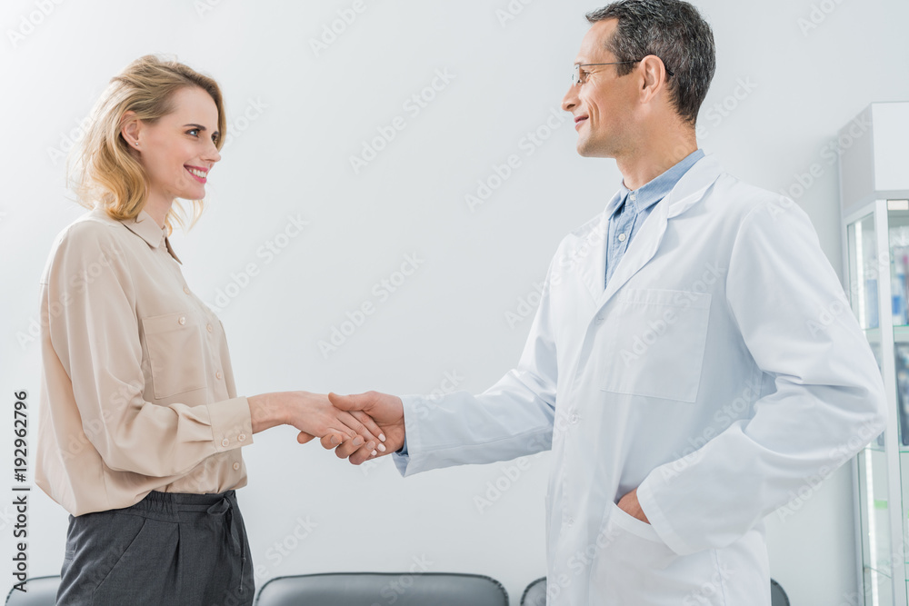 Male doctor and female patient shaking hands in modern dental clinic Male doctor and female patient shaking hands in modern dental clinic