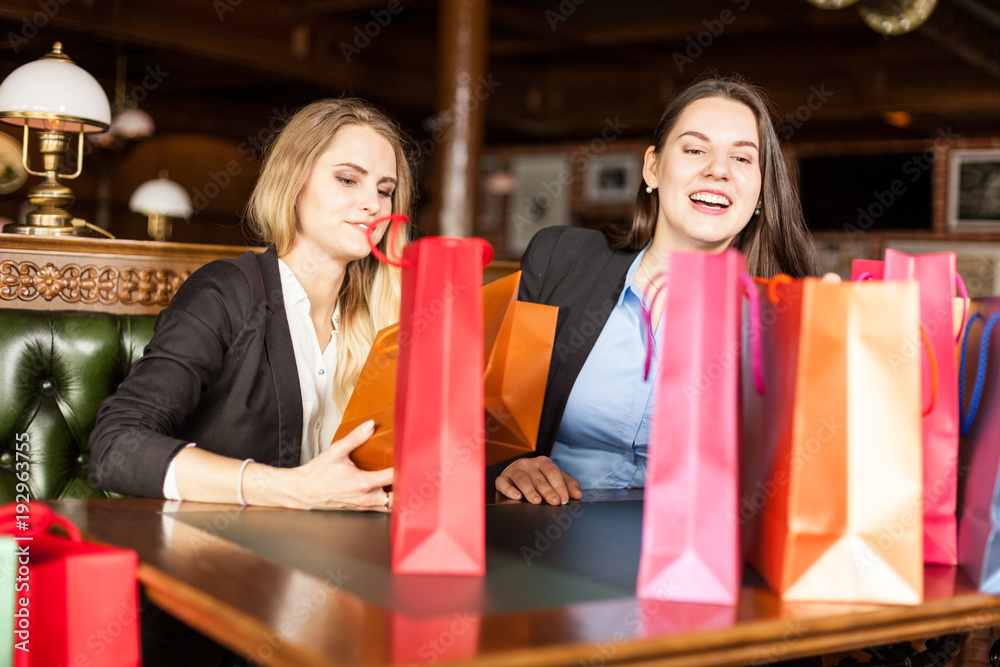 Two european adult woman have lots of shopping bags on a table and they having a good time Two european adult woman have lots of shopping bags on a table and they having a good time