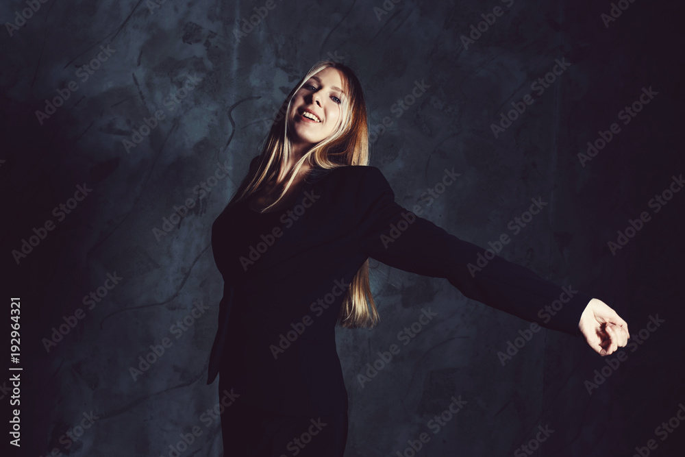 Attractive pretty young model posing against a dark studio background with copy space looking. Atomic blonde woman stands with widely spread arms. Cold cinematic style Attractive pretty young model posing against a dark studio background with copy space looking. Atomic blonde woman stands with widely spread arms. Cold cinematic style