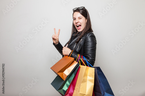 Winking girl with shopping bags shows two fingers peace