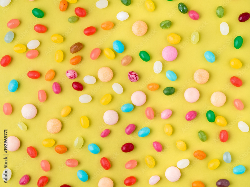 Many scattered colorful sweets, candies, lollipops on bright yellow background, top view Many scattered colorful sweets, candies, lollipops on bright yellow background, top view