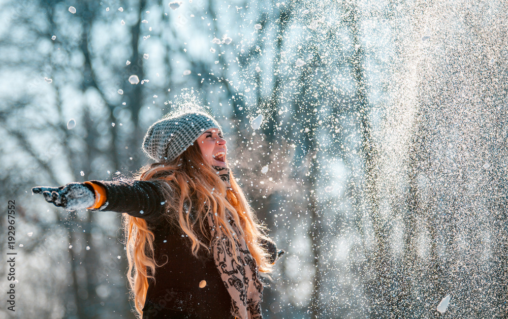 Obraz premium Smiling woman throwing snow in the air at sunny winter day