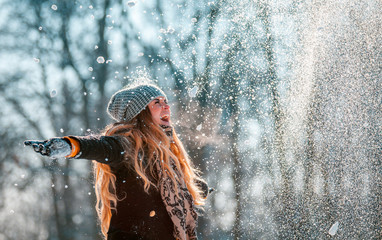 Smiling woman throwing snow in the air at sunny winter day