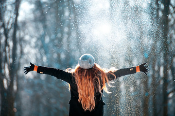 Young girl throwing snow in the air at sunny winter day, back view