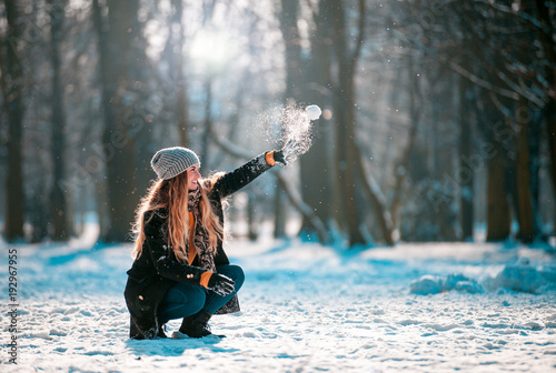 Young woman throwing snowball at sunny day in winter park photo