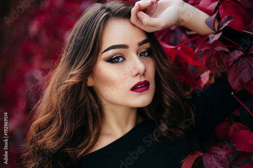 The beautiful girl stands near walll with leaves photo