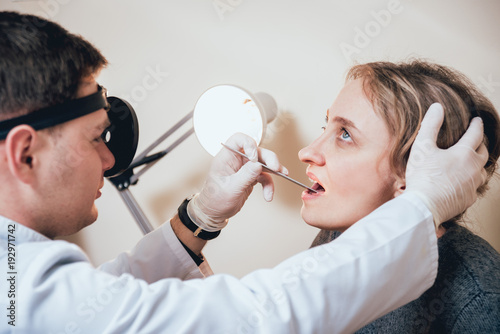 Otolaryngologist examines woman's throat with medical spatula. photo