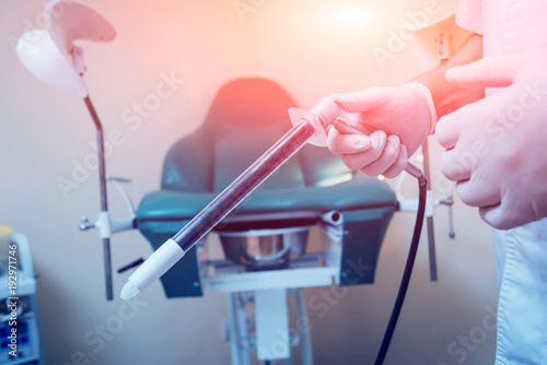 Proctologist holding an anoscope against a proctological chair.