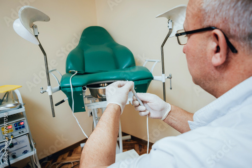 Proctologist holding an anoscope against a proctological chair. photo