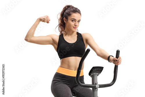 Teenage girl exercising on a cross-trainer machine and flexing her biceps
