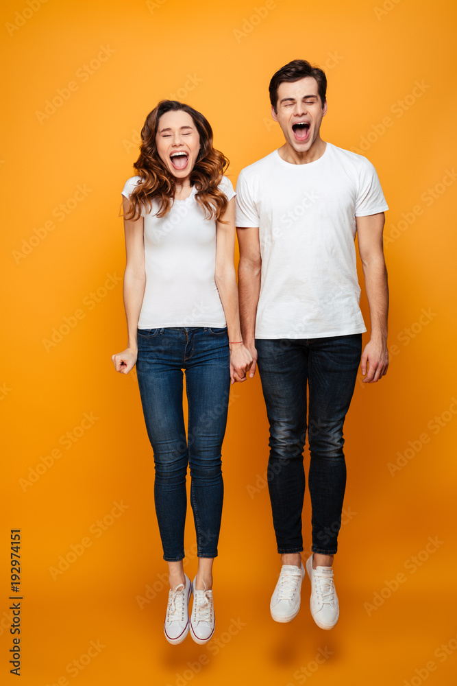 Full-length image of funny man and woman in casual posing on camera with closed eyes while jumping and screaming, isolated over yellow background Full-length image of funny man and woman in casual posing on camera with closed eyes while jumping and screaming, isolated over yellow background