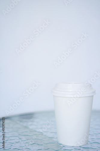 A white paper glass  one-time  for coffee is on the table. Background is blurred. Place for the title on the glass. Side view with copy space