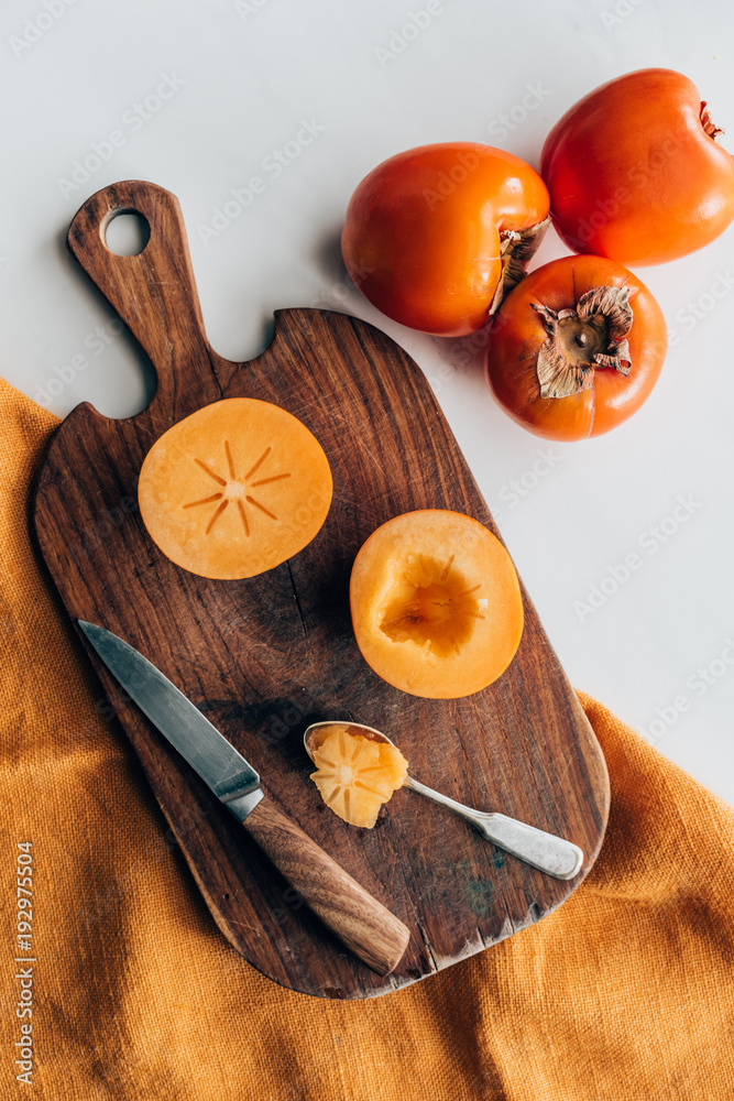 top view of persimmons on wooden board with knife and spoon top view of persimmons on wooden board with knife and spoon