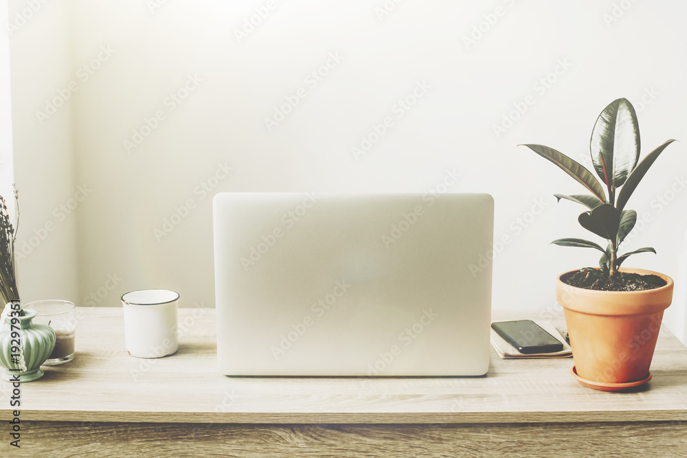 Laptop on wooden desktop with phone, notebook, coffee cup and plant in stylish modern room. Freelance concept. business workspace in home or office. stylish work place. working online